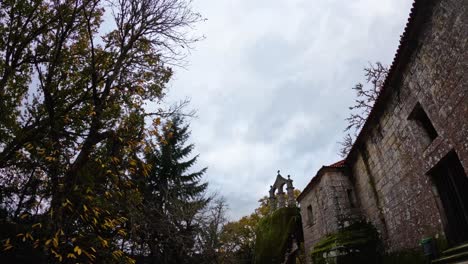 Beautiful-timelapse-of-the-cloudy-gray-sky-surrounded-by-trees,-nature-and-an-old-stone-construction-with-a-Christian-cross-on-top
