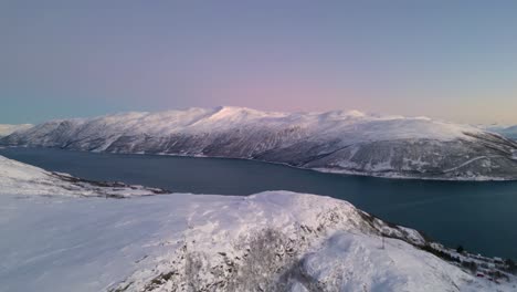 Aerial-view-of-Norwegian-fjords-at-sunset-with-snowy-mountains-and-blue-sea-in-Ersfjordvegen