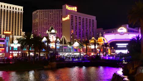 Colorful-evening-view-of-Harrah's-Hotel-and-Casino,-bustling-with-people-and-neon-lights-reflecting-in-the-water