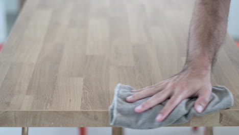 Person-cleaning-a-wooden-table-surface-with-a-cloth