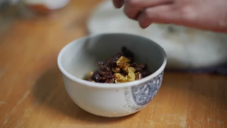 Freshly-soaked-and-diced-raisins-and-berries-moved-from-marble-cutting-board-into-bowl,-filmed-as-close-up-slow-motion-shot