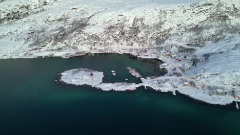 Aerial-view-of-Norwegian-fjords-and-Ersfjordvegen-village-with-snowy-mountains-and-parked-boats