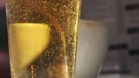 Cerveza-Dorada-En-Vaso,-Cámara-Lenta-De-Primer-Plano-En-Un-Bar-Iluminado-Por-El-Sol
