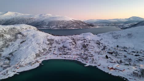 Stunning-aerial-view-of-Norwegian-fjords-and-Ersfjordvegen-village-with-snowy-mountains-and-blue-sea