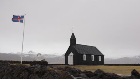 Schwarze-Kirche-Von-Budir-Und-Flagge-Islands-In-Nebliger-Berglandschaft