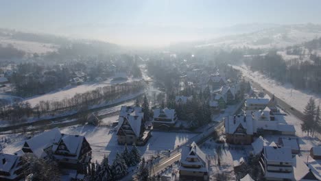 Tatra-Mountain-village,-traditional-cottages-in-snow-and-sunlight-aerial-view,-Poland
