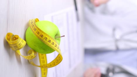 Vertical-video-of-Apple-and-Measure-tape-in-Focus,-Doctor-using-Smartphone-in-Blurred-background