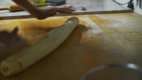 Hands-rolling-and-pressing-cinnamon-roll-dough-on-wooden-kitchen-bench,-filmed-as-close-up-handheld-shot