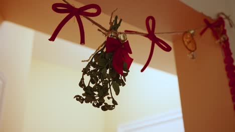Mistletoe-hangs-in-doorway,-with-red-bows-and-twine