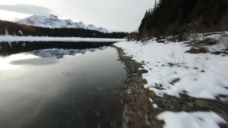 Snowy-Italian-mountains-reflected-in-alpine-lake,-fast-FPV-drone-shot