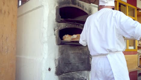 Baker-takes-out-loaves-of-bread-from-one-oven-and-puts-them-in-the-oven-above-at-the-Christmas-market-in-Meran---Merano,-South-Tyrol,-Italy