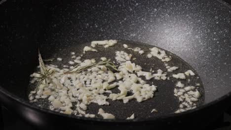 Garlic-Sizzling-In-Oil-With-Rosemary-Herbs-Over-Skillet