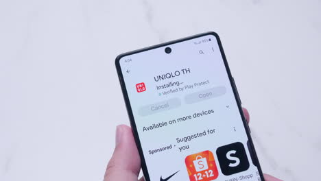 Hand-holding-a-smartphone-with-installing-UNIQLO-application-from-Google-play-store