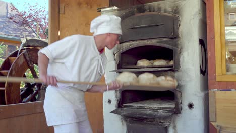 Baker-moving-loaves-of-bread-from-one-oven-to-another-one-at-the-Christmas-market-in-Meran---Merano,-South-Tirol,-Italy