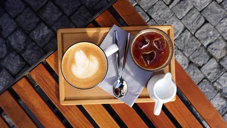 Top-down-view-of-ice-coffee-and-latte-cups-with-spoons-on-wooden-outdoor-table