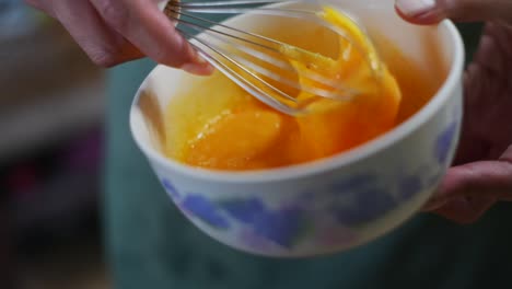 Raw-orange-egg-yolks-whisked-and-beaten-in-bowl-by-hand,-filmed-as-close-up-in-slow-motion