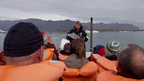 Guide-with-piece-of-melting-ice-talking-to-group-of-tourists-on-boat-tour---Jökulsárlón-Glacier-Lagoon-in-Iceland