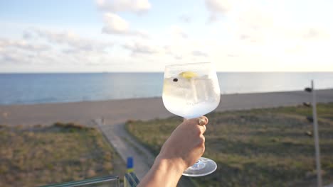 Cocktail-gin-and-tonic-in-a-terrace-held-by-a-woman-with-beautiful-and-amazing-sea-views-landscape