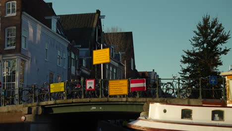 Blick-Vom-Amsterdamer-Kanal,-Hausboot,-Brücke-Mit-Fahrrädern-Und-Typischen-Häusern