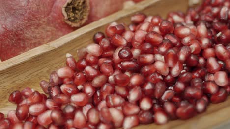 Close-up-panning-shot-of-pomegranate-seeds-inside-wooden-plate-juicing-and-using-fresh-ingredients-and-fresh-whole-pomegranates