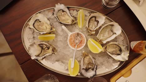 Top-down-view-of-oysters-plate-with-lemon-slices-placed-on-ice,-wooden-table