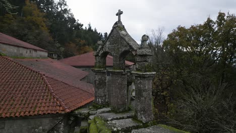 Circular-drone-aerial-shot-of-an-old-monastery-construction-surrounded-by-trees-and-nature-with-a-Christian-cross-on-top