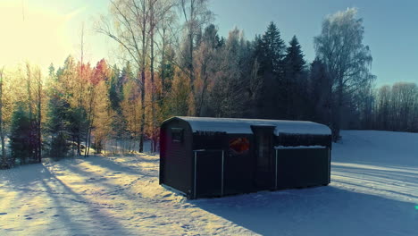 Golden-sunset-and-a-cabin-trailer-and-sauna-in-a-snowy-countryside---pullback-aerial-reveal