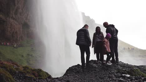 Touristen-Fotografieren-Auf-Einem-Felsen-Hinter-Dem-Vorhang-Aus-Fallendem-Wasser-Des-Seljalandsfoss-Wasserfalls-In-Island