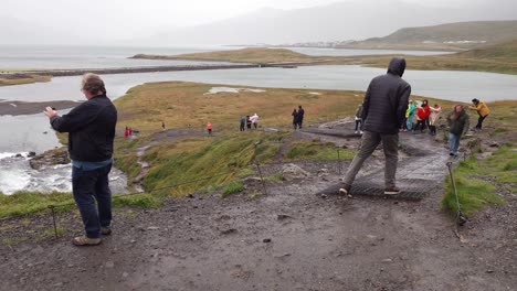 Tourist,-Der-An-Einem-Windigen-Tag-Auf-Der-Halbinsel-Snæfellsnes-In-Island-Ein-Foto-Auf-Dem-Wasserfall-Kirkjufellsfoss-Macht