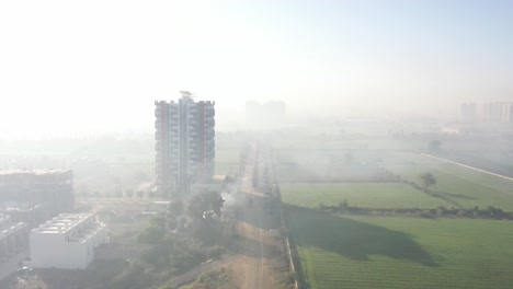 Luftdrohnenaufnahme-Von-Natürlichem-Nebel,-Die-Drohnenkamera-Bewegt-Sich-Vorwärts,-Wo-Wohnhäuser-Und-Große-Hochhäuser-Von-Vielen-Feldern-Umgeben-Sind