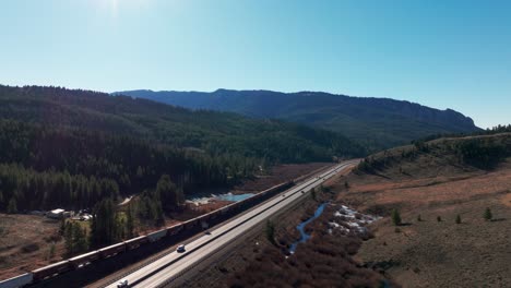 Aerial-view-of-BNSF-Railway-Train-traveling-alongside-a-highway-in-Montana