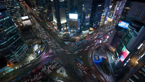 Cars-Passing-Through-Gangnam-Station-Intersection-at-Night,-Busiest-Street-in-Seoul-Downtown-with-High-Towering-Skyscrapers---top-down-view