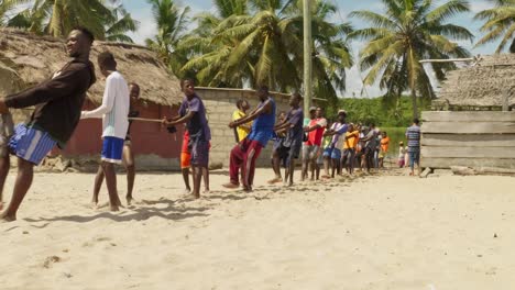 Young-men-pull-fishing-net-rope-up-to-sunny-sand-beach-in-Moree,-Ghana