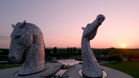 "Slow-orbit-drone-footage-of-the-Kelpies-in-Helix-Park,-capturing-the-sculptures'-details-against-a-stunning-purple-and-pink-sunset-sky