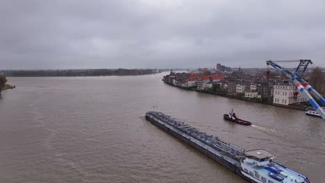 Passing-Dordrecht-city-on-either-side,-Crane,-tug-boat-and-vessel-sail