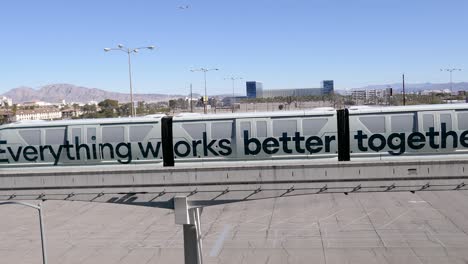 A-Las-Vegas-monorail-with-a-motivational-slogan-travels-under-a-clear-sky,-with-the-mountains-and-cityscape-in-the-background