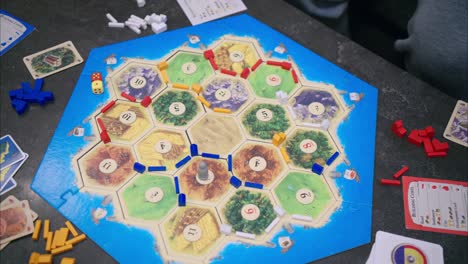 45-degree-overhead-view-of-Catan-gameplay-with-player's-hand-placing-the-robber-on-a-brick-tile-and-stealing-a-card-from-another-person's-hand