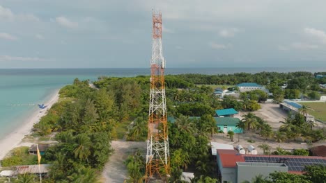 A-High-Angle-Shot-Of-A-Power-Transmitter-At-A-Coastal-Landscape-With-Buildings-And-Tropical-Trees