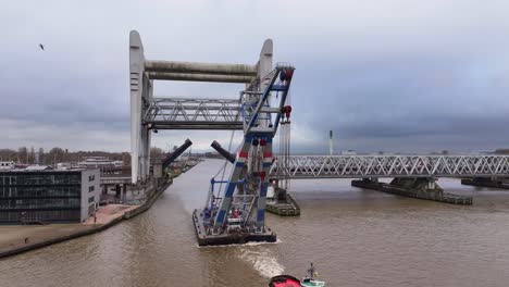 Industrial-crane-floats-through-railway-bridge-tugged-by-small-vessel
