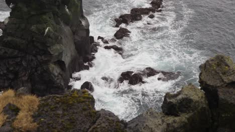 Dramatic-zoom-out-of-Atlantic-ocean-waves-splash-against-dark-rock-cliff