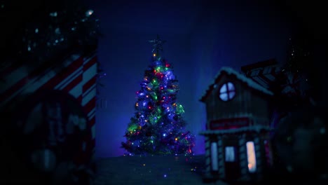 Camera-slowing-pushes-away-from-a-beautiful,-well-lit-Christmas-tree-sitting-behind-a-small,-cute-Christmas-village-that-sits-out-of-focus-in-front-of-camera