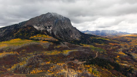 Dramatic-road-sunny-cloudy-autumn-Aspen-Tree-fall-colors-Kebler-Pass-aerial-cinematic-drone-snow-on-peaks-landscape-Crested-Butte-Gunnison-Colorado-early-fall-red-yellow-orange-Rocky-Mountains-forward