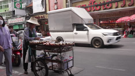 Street-Food-Vendor-with-Traditional-Hat-Selling-Food-in-Chinatown,-Bangkok,-Thailand