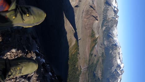 Vertikale-Aufnahme---Wanderer-Sitzt-Auf-Der-Klippe-Und-Blickt-Auf-Die-Felsigen-Berge-In-British-Columbia,-Kanada