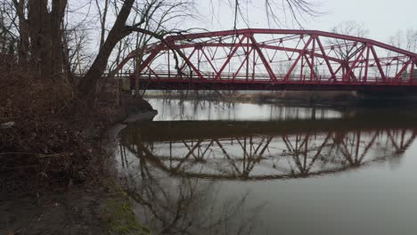 Eine-Kleine,-Malerische-Bogenbrücke-Aus-Rotem-Stahl,-Von-Einem-Kleinen-Park-Aus-Gesehen,-Die-An-Einem-Regnerischen,-Trostlosen-Vorfrühlingstag-Einen-Kleinen-Fluss-Im-Norden-Des-Bundesstaates-New-York-überquert