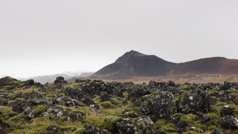 Man-jump-on-moss-covered-lava-field-rock,-dark-mountain-contour-in-background