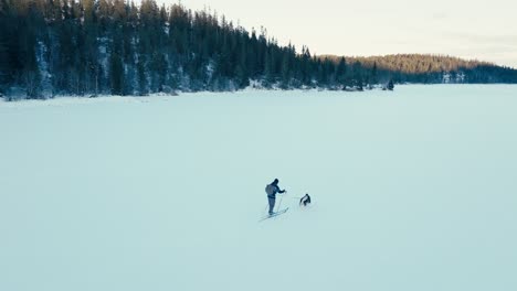 Alaskan-Malamute-Zieht-Mann-Beim-Skifahren-Im-Verschneiten-Zugefrorenen-See-Im-Winter
