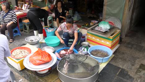 Woman-prepares-raw-fish-for-eager-customers-at-busy-wet-market-stall