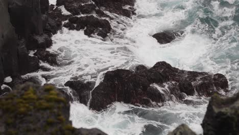 Close-up-of-huge-powerful-ocean-waves-hit-against-black-shoreline-cliff
