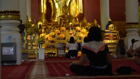 Gente-Sentada-En-El-Suelo-Rezando-Frente-A-La-Enorme-Estatua-Dorada-De-Buda-En-Wat-Phra-Singh